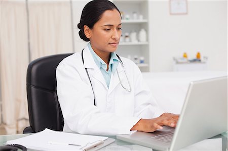 female doctor serious - Serious practitioner sitting at her desk while working with her laptop Stock Photo - Premium Royalty-Free, Code: 6109-06006905