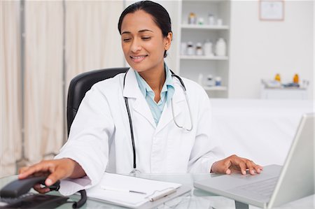 stethoscope computer - Smiling doctor hanging up her phone while working on her laptop Stock Photo - Premium Royalty-Free, Code: 6109-06006913