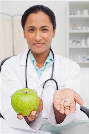 Relaxed nutritionist holding a delicious green apple and vitamins Stock Photo - Premium Royalty-Free, Code: 6109-06006928