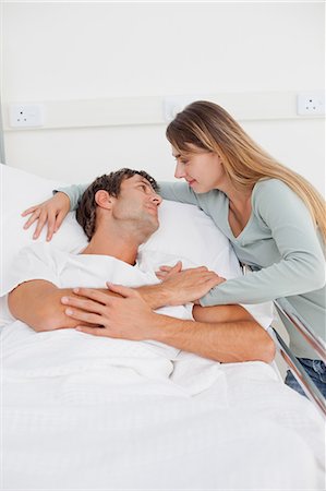 patient happy in bed - Patient détendu, allongé dans un lit d'hôpital, tout en étant salué par son épouse mignonne Photographie de stock - Premium Libres de Droits, Code: 6109-06007071