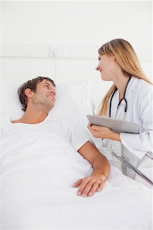 patient happy in bed - Souriant médecin examinant son patient tout debout avec un presse-papiers Photographie de stock - Premium Libres de Droits, Code: 6109-06007085