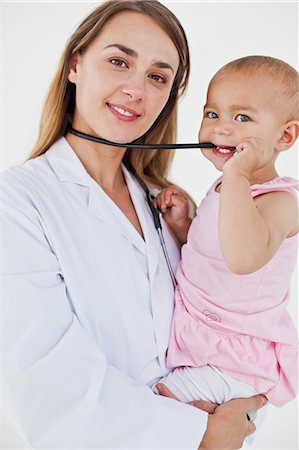 female doctor and child patient - Lovely baby chewing the stethoscope of the nurse who is holding her Stock Photo - Premium Royalty-Free, Code: 6109-06007094