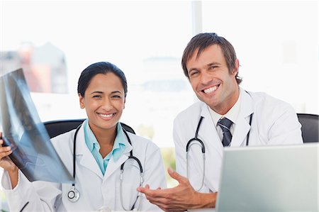 simsearch:6109-06006829,k - Doctors looking at the camera while smiling and sitting at a desk with a chest x-ray Foto de stock - Sin royalties Premium, Código: 6109-06007004