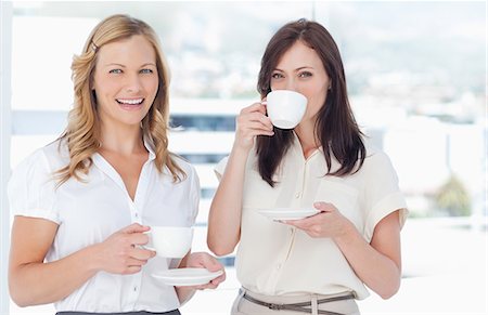 Woman looking ahead while smiling as she stands next to her friend who is drinking a cup of tea Stock Photo - Premium Royalty-Free, Code: 6109-06007174