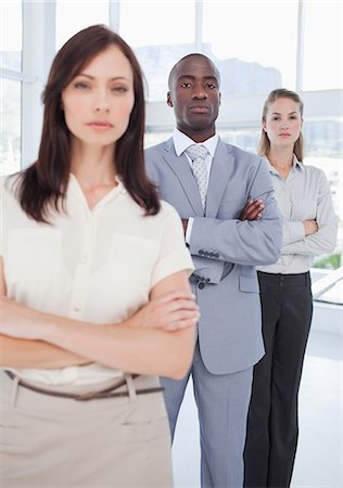 simsearch:6109-06007199,k - Serious man and a woman with their arms crossed standing behind their co-worker with focus on the man and woman Foto de stock - Royalty Free Premium, Número: 6109-06007196