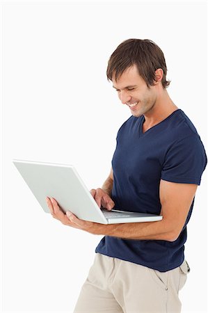 simsearch:6109-06007150,k - Smiling man working with a laptop while standing up against a white background Foto de stock - Sin royalties Premium, Código: 6109-06007133