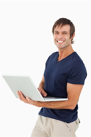 Happy man holding a laptop while looking at the camera against a white background Stock Photo - Premium Royalty-Free, Code: 6109-06007134