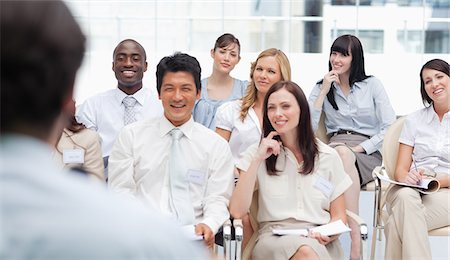 simsearch:6109-06007215,k - Smiling colleagues looking ahead of them as they watch a brown haired businessman Stock Photo - Premium Royalty-Free, Code: 6109-06007243