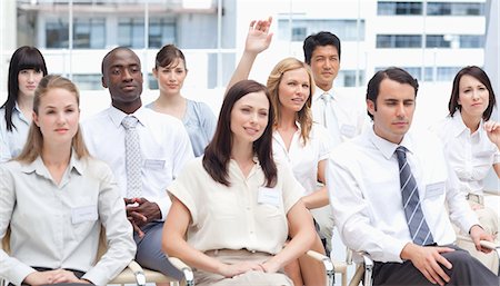 domanda - Blonde haired woman raising her arm as she sits in a group of her colleagues Fotografie stock - Premium Royalty-Free, Codice: 6109-06007208