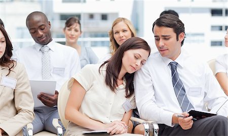 Man looking at his female colleague as she is sleeping on his shoulder while they sit in a group Stock Photo - Premium Royalty-Free, Code: 6109-06007225