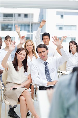 A group of co-workers raising their hands as they watch as speaker Stock Photo - Premium Royalty-Free, Code: 6109-06007229