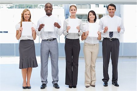 people holding placard - Business team smiling as they hold white sheets in front of them Stock Photo - Premium Royalty-Free, Code: 6109-06007352