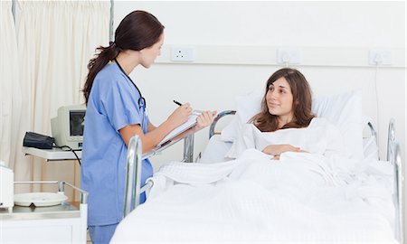 patient on bed for hospital - Nurse holding a clipboard as she talks with a patient who is lying in bed Stock Photo - Premium Royalty-Free, Code: 6109-06007354