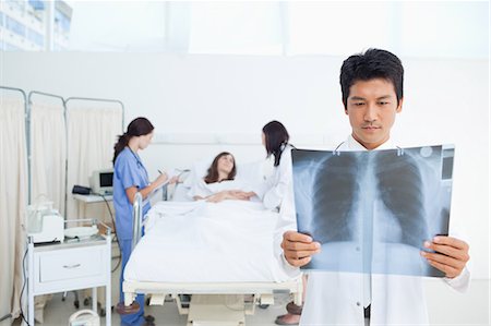 patient happy in bed - Doctor looking at an x-ray scan in front of him while his colleagues are examing a patient Stock Photo - Premium Royalty-Free, Code: 6109-06007371