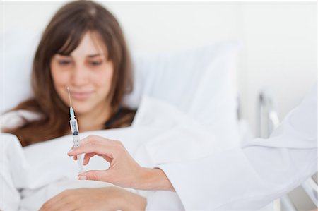 Woman looking at a syringe as it is held ahead of her as she lies in a bed Foto de stock - Royalty Free Premium, Número: 6109-06007382