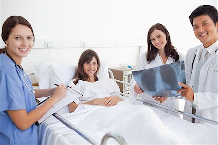 patient happy in bed - Smiling doctors accompanied by a nurse looking ahead as they hold an x-ray scan with a patient Stock Photo - Premium Royalty-Free, Code: 6109-06007387