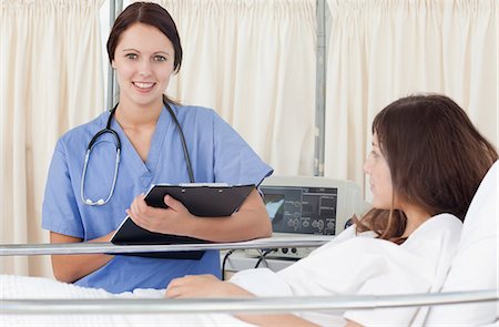 patient and nurse and happy - Smiling nurse looking in front of her while holding a clipboard next to the bed of a patient Foto de stock - Sin royalties Premium, Código: 6109-06007388