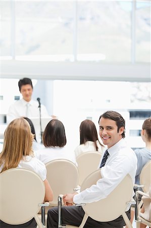 smiling - Happy businessman looking behind him as he sits with his colleagues during a presentation Stock Photo - Premium Royalty-Free, Code: 6109-06007325