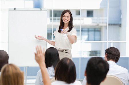 female raising her hand - Woman smiling as she gestures to a member of the audience that has her hand raised Stock Photo - Premium Royalty-Free, Code: 6109-06007335