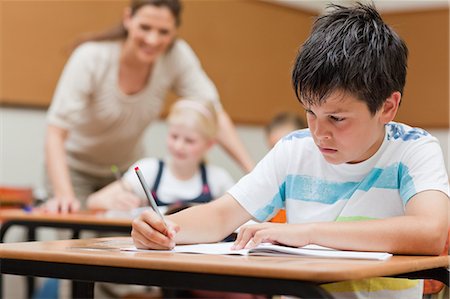 devoir (école) - Jeune écolier avec l'enseignant et condisciple en arrière-plan Photographie de stock - Premium Libres de Droits, Code: 6109-06007438