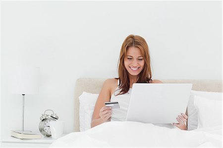 shopaholic bedroom - Smiling redheaded using her credit card online Stock Photo - Premium Royalty-Free, Code: 6109-06194501