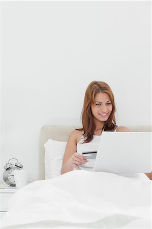 shopaholic bedroom - Close-up of a redheaded sitting on her bed while using her credit card online Stock Photo - Premium Royalty-Free, Code: 6109-06194505