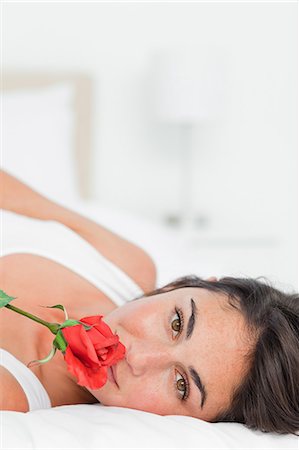 Gros plan d'une belle jeune fille allongée sur le dos tout en sentant une rose Photographie de stock - Premium Libres de Droits, Code: 6109-06194994