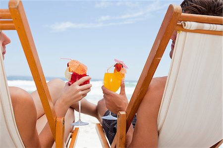 rear - Rear view of a young couple holding their cocktails while sitting on deck chairs Foto de stock - Sin royalties Premium, Código: 6109-06195246