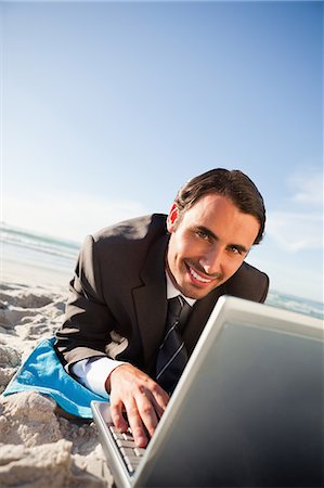 simsearch:6109-06195355,k - Homme d'affaires souriant à l'aide d'un ordinateur portable tout en se trouvant sur la plage Photographie de stock - Premium Libres de Droits, Code: 6109-06195349