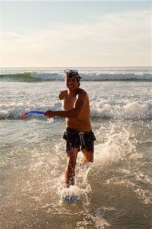 snorkeling mask - Young man running in the water while smiling Stock Photo - Premium Royalty-Free, Code: 6109-06195381