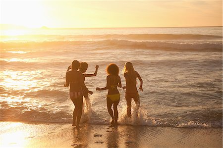 friends beach sunset - Young women getting in the water at sunset Stock Photo - Premium Royalty-Free, Code: 6109-06195387