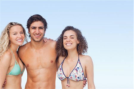 Three friends smiling as they hold each other while wearing swimsuits Stock Photo - Premium Royalty-Free, Code: 6109-06195472