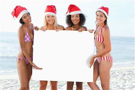 Four friends present a blank poster while wearing Santa hats Foto de stock - Sin royalties Premium, Código: 6109-06195636