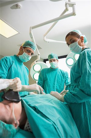 serious surgeon with mask - High view of a surgical team operating while looking at camera Stock Photo - Premium Royalty-Free, Code: 6109-06195897