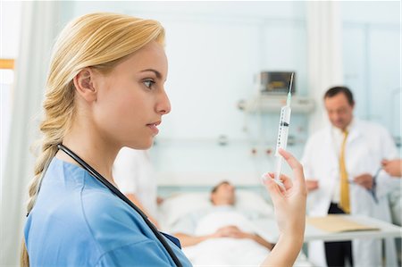 Blonde nurse looking at a syringe while holding it Stock Photo - Premium Royalty-Free, Code: 6109-06195942