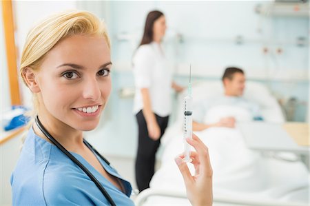 doctors inside the patients room photo - Nurse holding a syringe while smiling Stock Photo - Premium Royalty-Free, Code: 6109-06195944