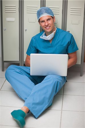 Surgeon sitting on the floor of a locker while holding a laptop Foto de stock - Sin royalties Premium, Código: 6109-06196054