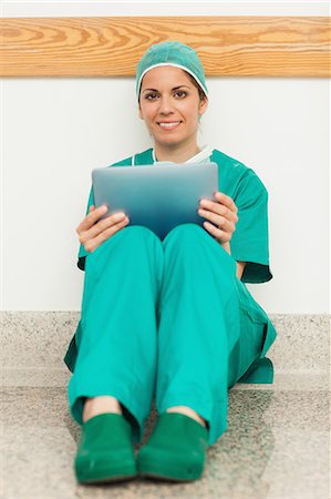 simsearch:6109-06196086,k - Smiling woman surgeon sitting in a hallway while using a tactile tablet Foto de stock - Royalty Free Premium, Número: 6109-06196083