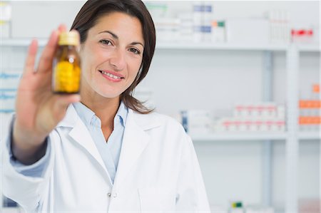 simsearch:6109-08537870,k - Smiling female pharmacist showing pills and standing in a pharmacy Stock Photo - Premium Royalty-Free, Code: 6109-06196147