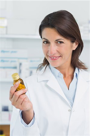 simsearch:693-05553326,k - Smiling female pharmacist holding a bottle of pills in a pharmacy Foto de stock - Sin royalties Premium, Código: 6109-06196153