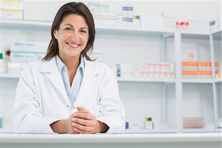 Pharmacien de femme souriant derrière un comptoir en joignant ses mains Photographie de stock - Premium Libres de Droits, Code: 6109-06196158