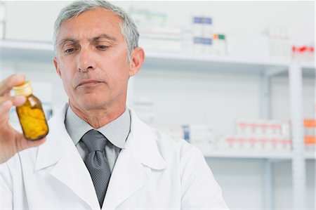 simsearch:6109-06196164,k - Male pharmacist looking at a flask of pills Stock Photo - Premium Royalty-Free, Code: 6109-06196169