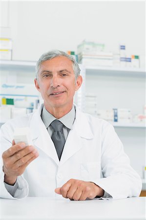 pharmacist looking at camera - Smiling pharmacist holding a box full of pills Stock Photo - Premium Royalty-Free, Code: 6109-06196177