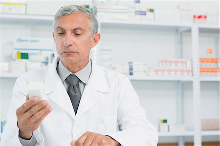 simsearch:6109-08537870,k - Serious pharmacist looking at a box full of pills Stock Photo - Premium Royalty-Free, Code: 6109-06196175