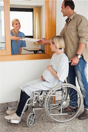simsearch:6109-06196003,k - Nurse giving a paper to a man and a pregnant woman in a wheelchair Foto de stock - Sin royalties Premium, Código: 6109-06196107