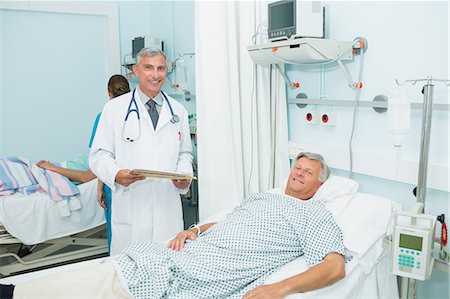 simsearch:6109-06195920,k - Smiling male doctor with a happy patient in a bed ward Foto de stock - Sin royalties Premium, Código: 6109-06196256