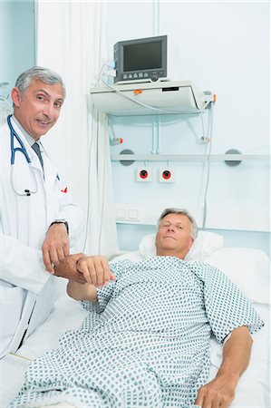 disease hospital ward - Smiling doctor measuring the pulse of a male patient Stock Photo - Premium Royalty-Free, Code: 6109-06196265