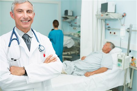 Happy doctor with his arms crossed standing in a bed ward Stock Photo - Premium Royalty-Free, Code: 6109-06196274