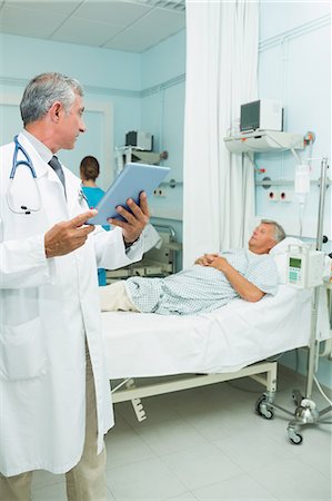 simsearch:6109-06196338,k - Serious doctor using a tactile tablet while looking at a patient in a bed ward Stock Photo - Premium Royalty-Free, Code: 6109-06196287