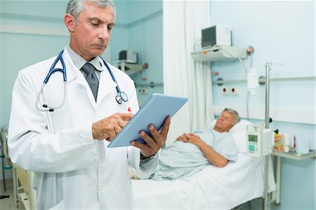 Médecin sérieux en utilisant une tablette tactile en se tenant debout dans une salle d'hôpital lit Photographie de stock - Premium Libres de Droits, Code: 6109-06196284